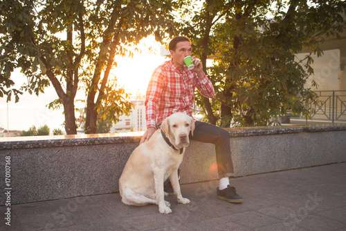 Young men relaxing in the mornin city with cup of coffee or tea and labrdor dog 