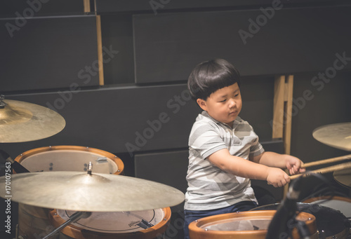 Little caucasian boy drummer playing the drum set in studio
