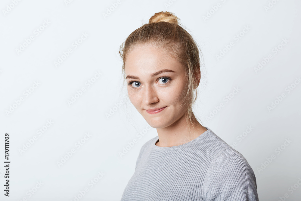 Headshot of adorable blue-eyed female with light hait tied in knot, looking with delightful expression into camera, going to have walk. Female teenager resting at home after hard working day Headshot of adorable blue-eyed female with light hait tied in knot, looking with delightful expression into camera, going to have walk. Female teenager resting at home after hard working day