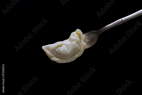 Ukrainian and Russian dishes - vareniki or dumplings with mashed potatoes or cottage cheese on a fork on a black background