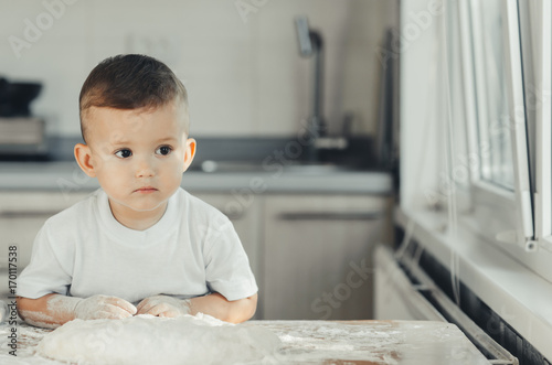 The boy in the kitchen covered in flour sitting at the table photo