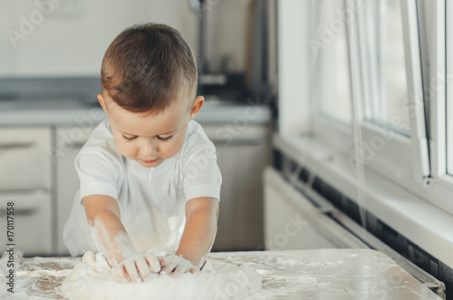 The little Boy in the kitchen hard kneads the dough