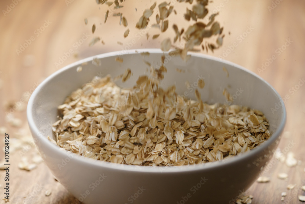 oat flakes fall in white bowl on wood table oat flakes fall in white bowl on wood table