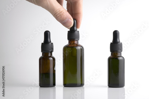 Isolated hand holding a medical brown drop bottle over a white b