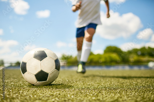 Low section portrait of unrecognizable teenage boy kicking ball during football practice, focus on ball lying on grass