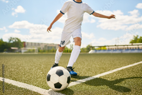 Fototapeta Naklejka Na Ścianę i Meble -  Portrait of unrecognizable teenage boy kicking ball during football practice in field outdoors
