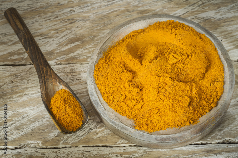 Turmeric powder in bowl and spoon on wooden table (curcuma longa) Turmeric powder in bowl and spoon on wooden table (curcuma longa)