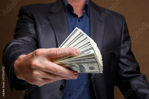 A man in a gray jacket is holding a lot of money in his hand