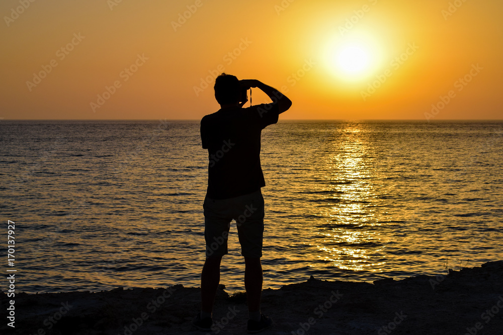 Silhouette of a man taking photos of the sunset over the Mediterranean Sea from Formentera Island, south of Ibiza Spain