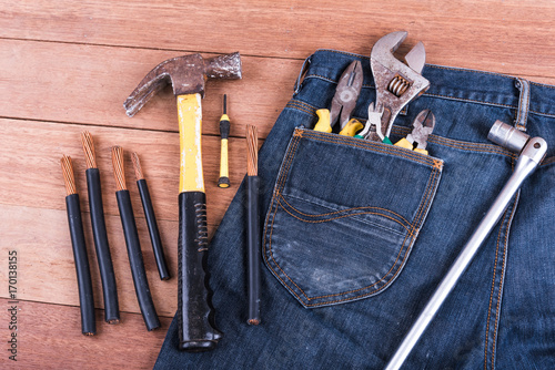 Several tools in a denim workers pocket on wood planks