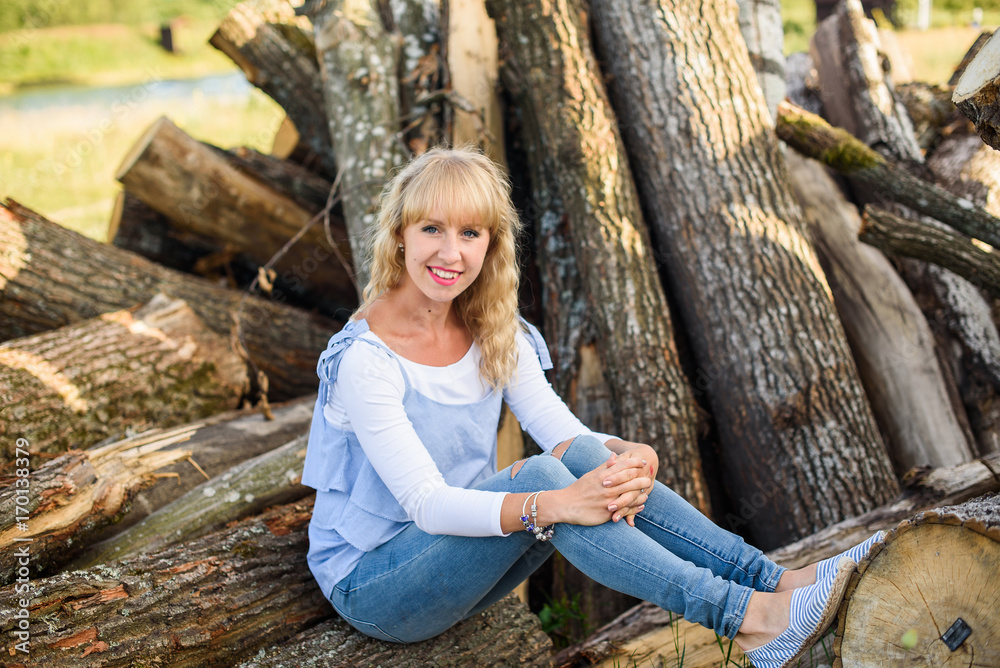 A young blonde teenage girl with a beautiful smile on a huge log pile. Full of happiness outdoors A young blonde teenage girl with a beautiful smile on a huge log pile. Full of happiness outdoors