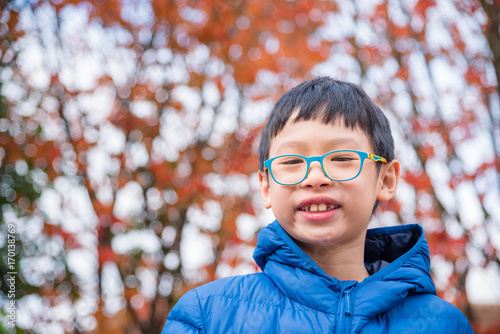 Young asian boy smiling at camera in red autumn park