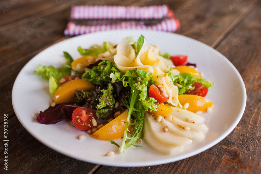 Green salad with cheese and fruits on plate. Lettuce, fresh vegetables decorated pine nuts, avocado, pearch and pear, serving in restaurant close up Green salad with cheese and fruits on plate. Lettuce, fresh vegetables decorated pine nuts, avocado, pearch and pear, serving in restaurant close up