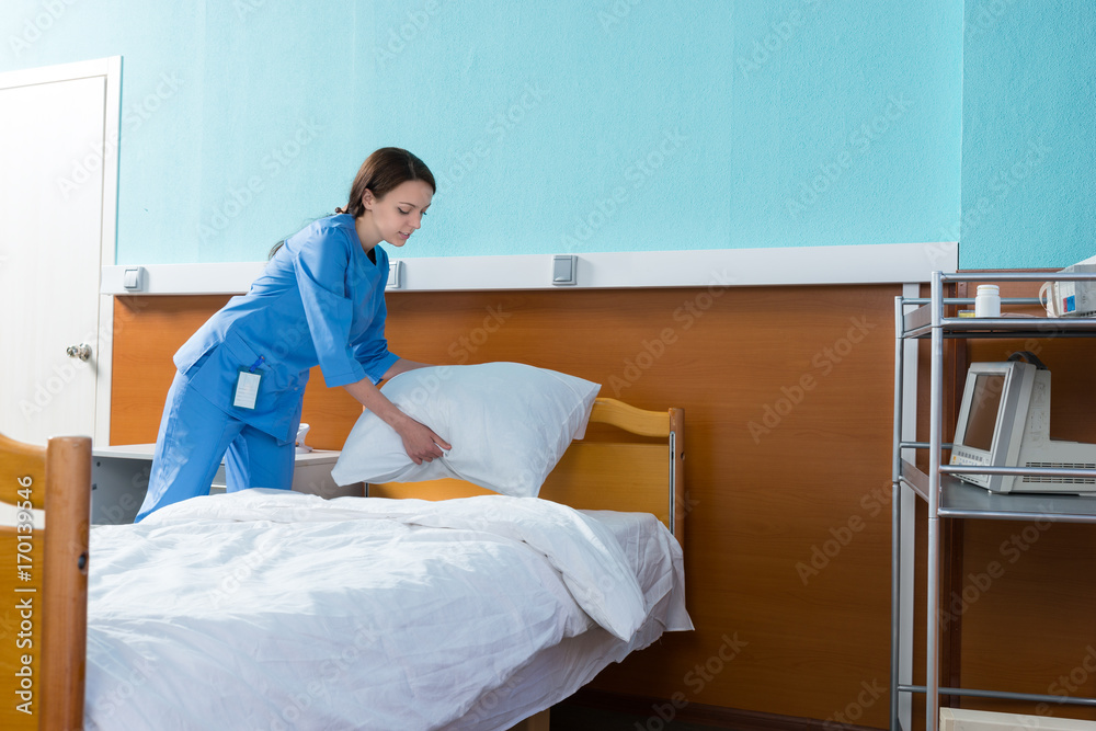 Female nurse holds a white pillow over the hospital bed in the hospital ward