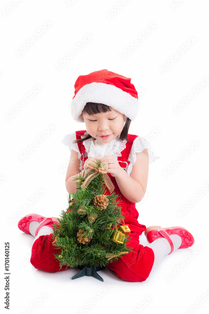 Little asian cute girl wearing santa dress sitting on the floor with christmas tree