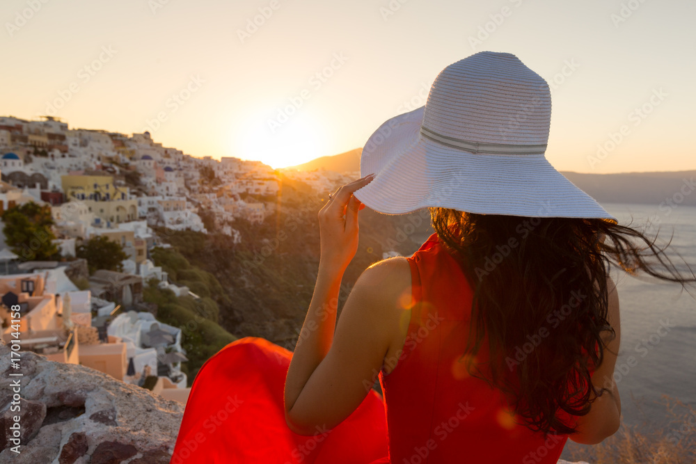 Santorini travel tourist brunette woman in red dress visiting famous white Oia village.