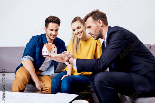 Handsome experienced real estate agent showing house model to young couple