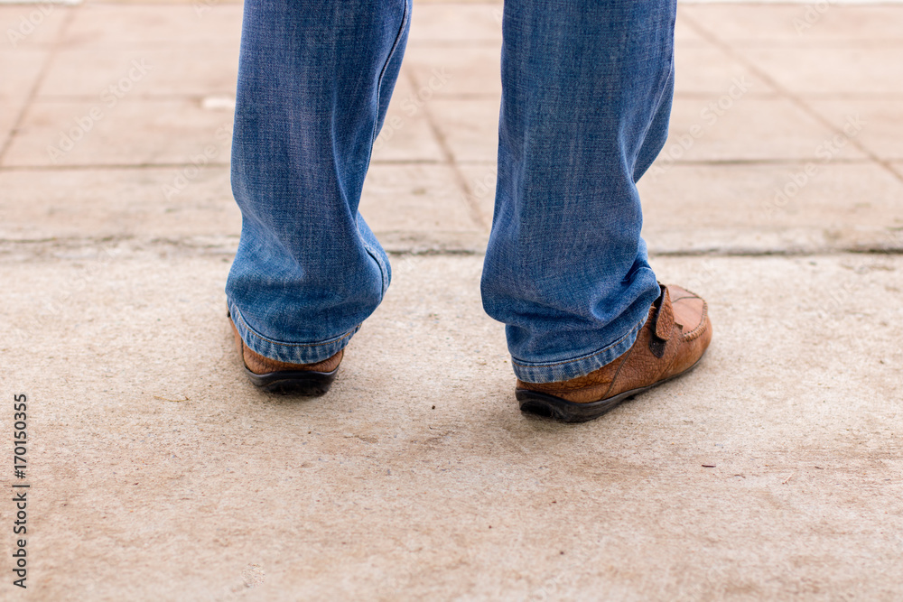 Young fashion man's legs in blue jeans and brown boots on concrete floor with copy space , old fashion leather shoes