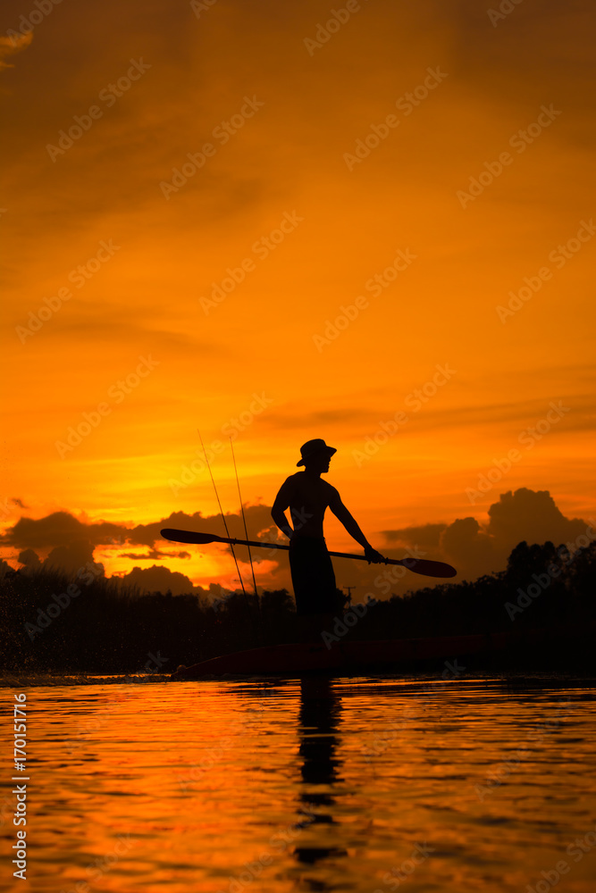 Silhouette of  fisherman standing on boat,hold paddle and paddle with a splash of water on sunset background.