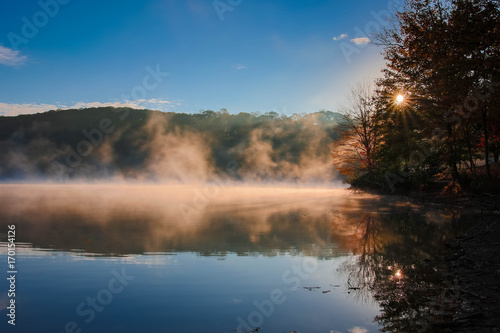 sunburst at sunrise with foggy lake with autumn trees in background