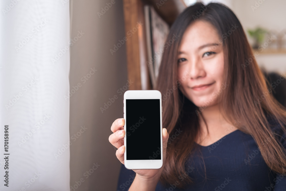 Mockup image of a beautiful Asian woman holding and showing white mobile phone with blank black screen in modern cafe Mockup image of a beautiful Asian woman holding and showing white mobile phone with blank black screen in modern cafe