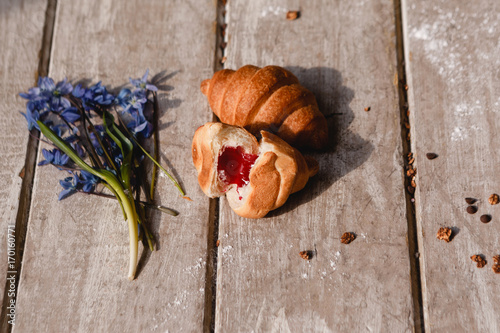 Delicious croissant on wooden background. Sweet breakfast from cookie and granola with spring blue snowdrops nearby. Morning fresh and tasty meal. Food photography
