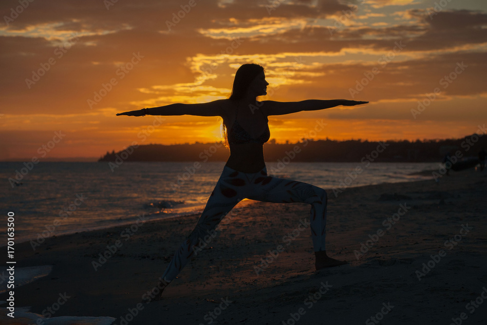 young woman practicing yoga warrior and hero pose at sunset, sunrise . Zen wellness and wellbeing concept.