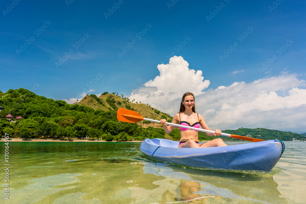 Happy young woman paddling a canoe on shallow water during vacation in an idyllic travel destination from Indonesia