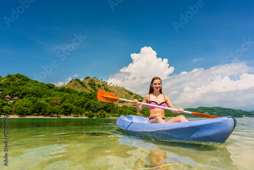 Happy young woman paddling a canoe on shallow water during vacation in an idyllic travel destination from Indonesia