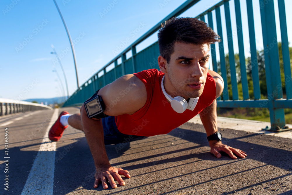 Fototapeta premium Portrait of young athlete man doing push ups on bridge.