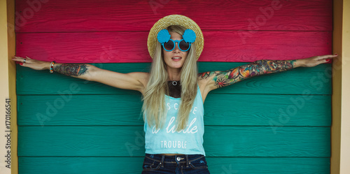 Beautiful young woman hipster with a tattoo in sunglasses and a hat on a bright coloured background. Beach style