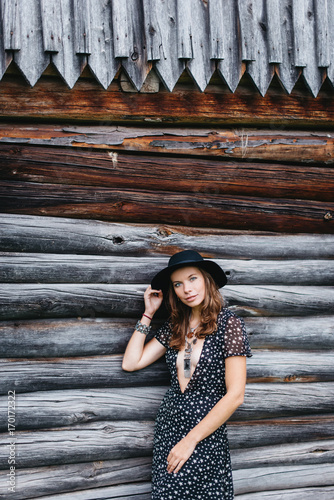beautiful girl in black hat and black dress with stars on a wooden log wall background. Toning