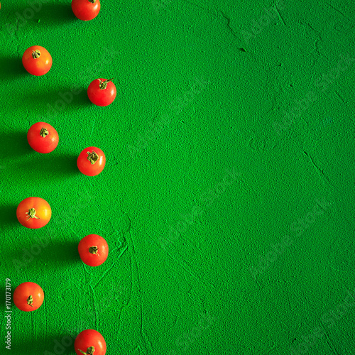 Red tomatoes cherry, scattered in a chaotic manner on a green background. Food background.