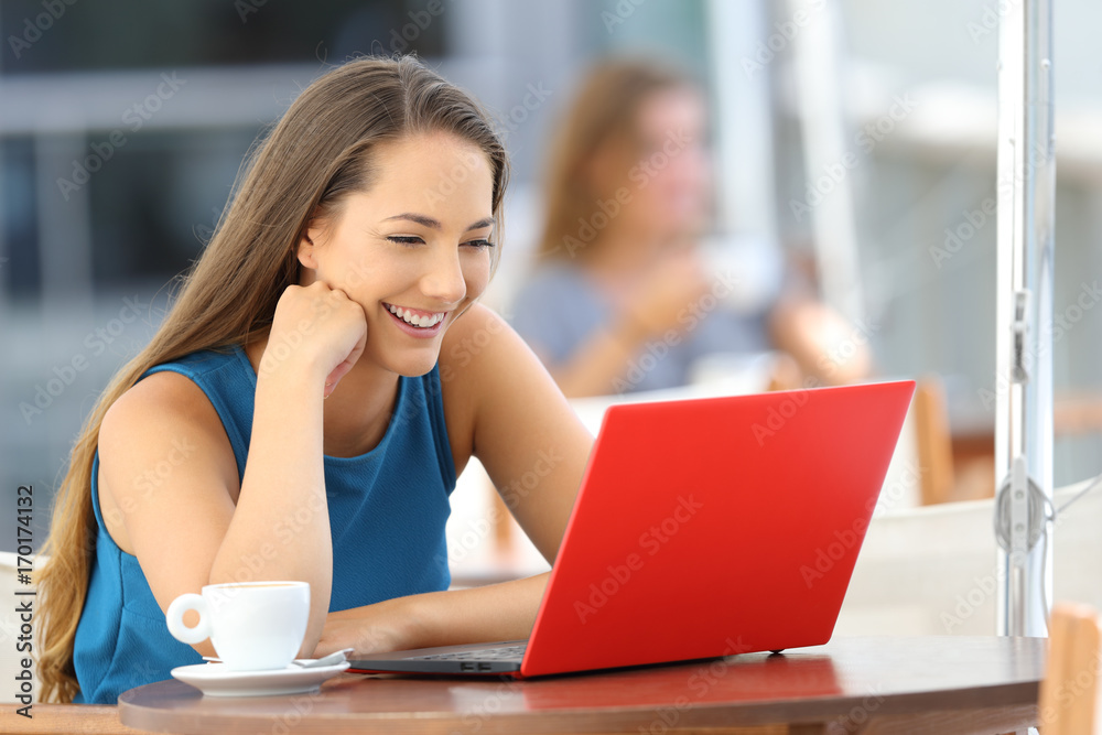 Happy woman watching media in a laptop in a bar