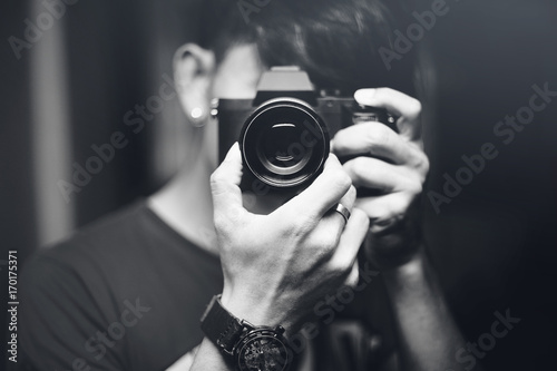 hipster image. a man use mirrorless camera for taking himself in the mirror. male photographer taking a picture with camera. black and white picture style. selective focus