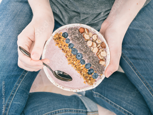 Eating healthy breakfast bowl. Buckwheat smoothie porrige, fresh berries, seeds and nuts, bee pollen in white ceramic bowl in woman hands. Clean eating, dieting, detox, vegetarian food concept