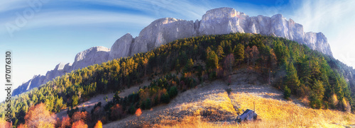 Beautiful scenic golden autumn landscape of majestic Bolshoy Tkhach rocky mountain peak under blue sky at sunrise with wooden tourist hut on foreground. Panoramic scenery of Caucasus, Russia photo