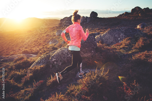 Athletic woman jogging around on rough terrain at sunset. Sport tight clothes. Intentional motion blur.