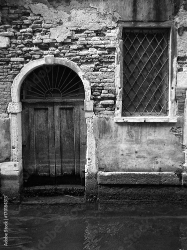 old door in venice opening on to a canal with stepe eroded bricks and square window photo