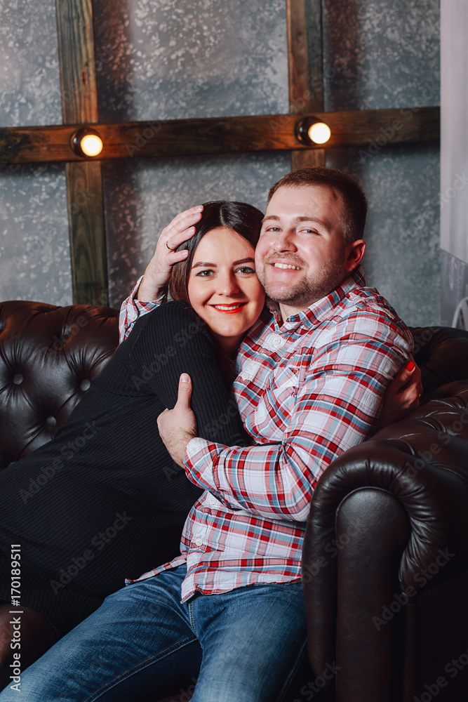 Future parents embrace sitting on the couch - pregnancy, rest, people and expectation concept