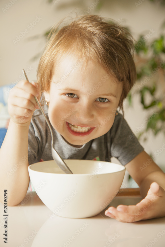 Happy cute little girl laughing and having breakfast muesli with milk at home in the kitchen (healthy food, eating, children, childhood concept ) Happy cute little girl laughing and having breakfast muesli with milk at home in the kitchen (healthy food, eating, children, childhood concept )