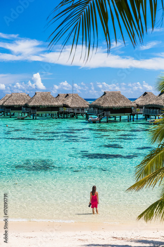 Luxury beach travel vacation woman in Tahiti. Tourist enjoying ocean water at overwater bungalow hotel villas in French Polynesia, Moorea island in south pacific, famous getaway destination.