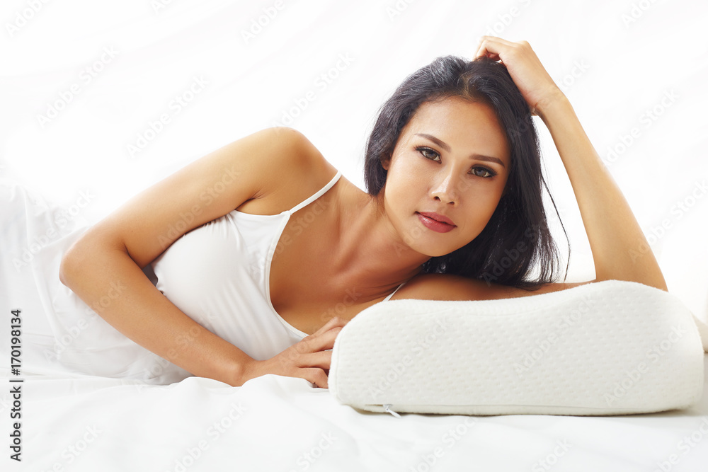 Close up portrait young female model resting n the white bed against white background Close up portrait young female model resting n the white bed against white background