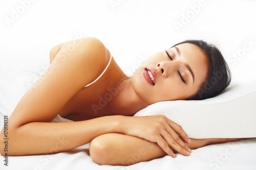 Close up portrait young female model resting n the white bed against white background