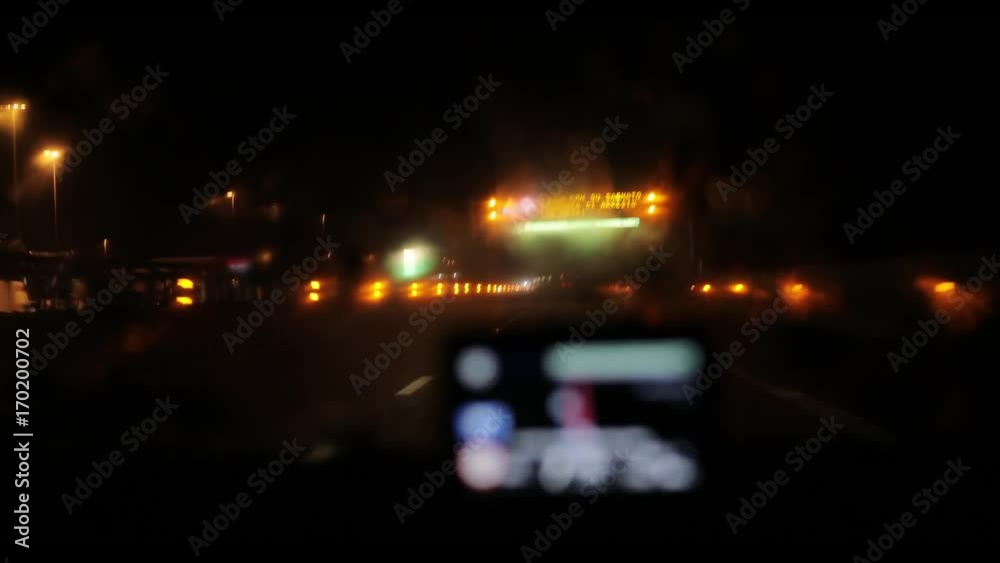 Night road from inside car 4k through defocused GPS navigation device screen. Passing electronic sign board with warning on wet slippery highway in Italy or Switzerland view from drivers perspective Night road from inside car 4k through defocused GPS navigation device screen. Passing electronic sign board with warning on wet slippery highway in Italy or Switzerland view from drivers perspective