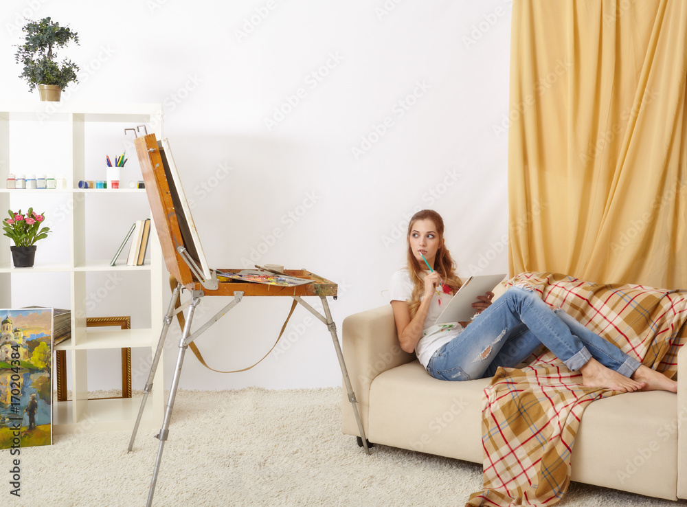 Painter female with wooden sketchbook sitting on sofa and painting Painter female with wooden sketchbook sitting on sofa and painting