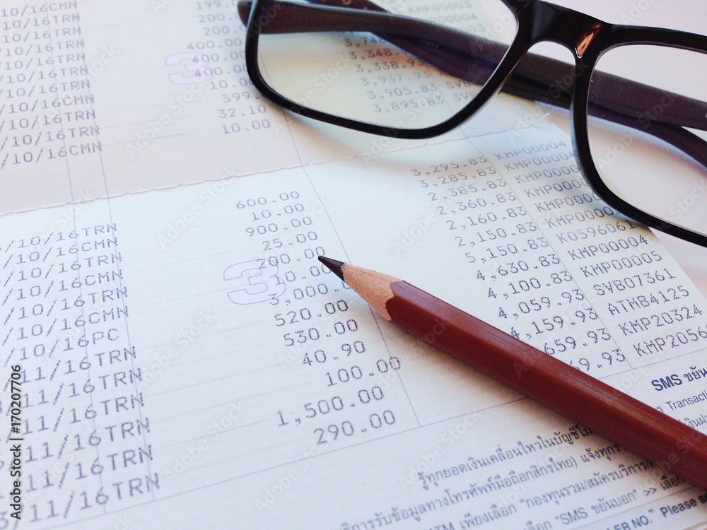 Business, finance, saving money, banking, loan, investment, taxes or accounting concept : Pen and eyeglasses on saving account book or financial statement Business, finance, saving money, banking, loan, investment, taxes or accounting concept : Pen and eyeglasses on saving account book or financial statement