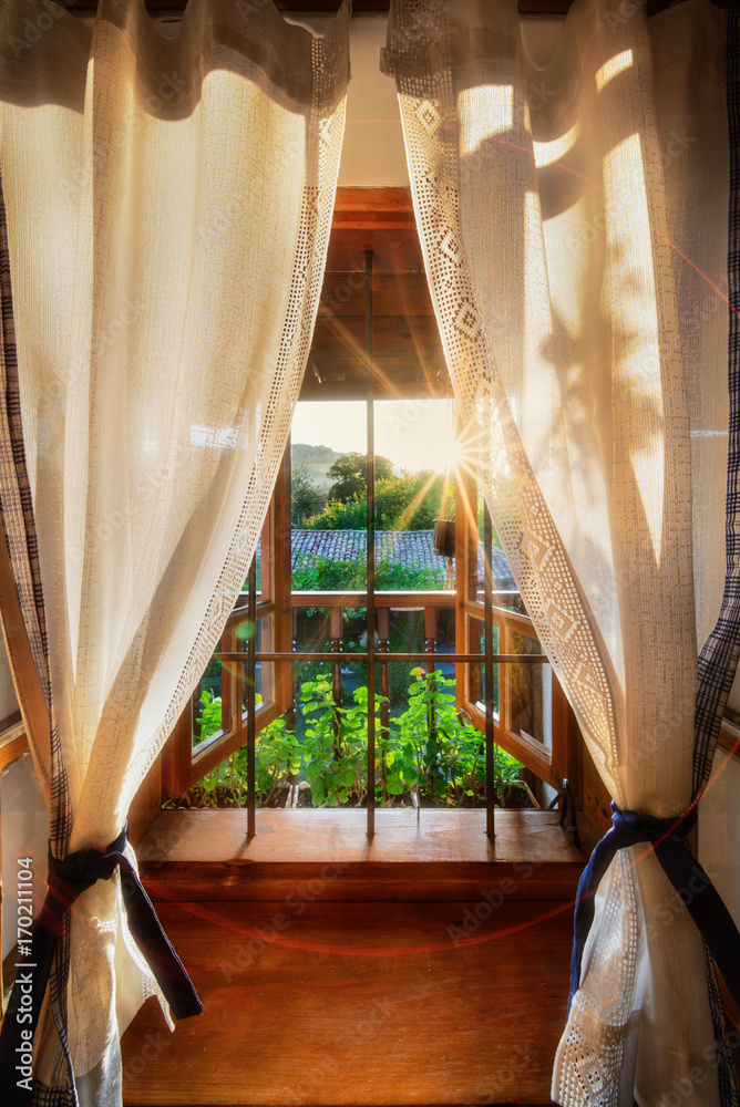 Late summer mountain view out of a romantic little window with drapes and lots of wooden elements during sunset