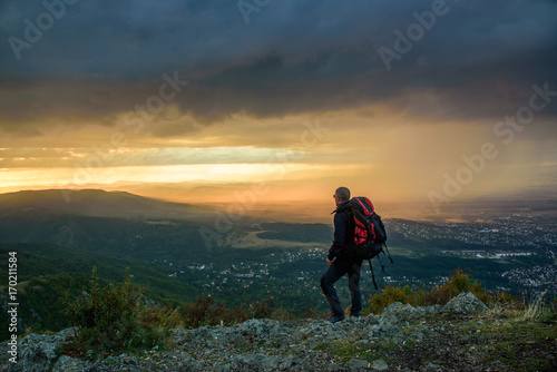 Amazing sunset on a mountain top - man with alpine equipment enjoying the breathtaking view under the stormy sky