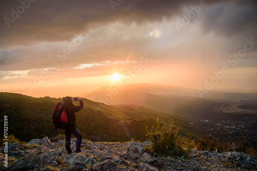 Amazing sunset on a mountain top - man with alpine equipment enjoying the breathtaking view under the stormy sky